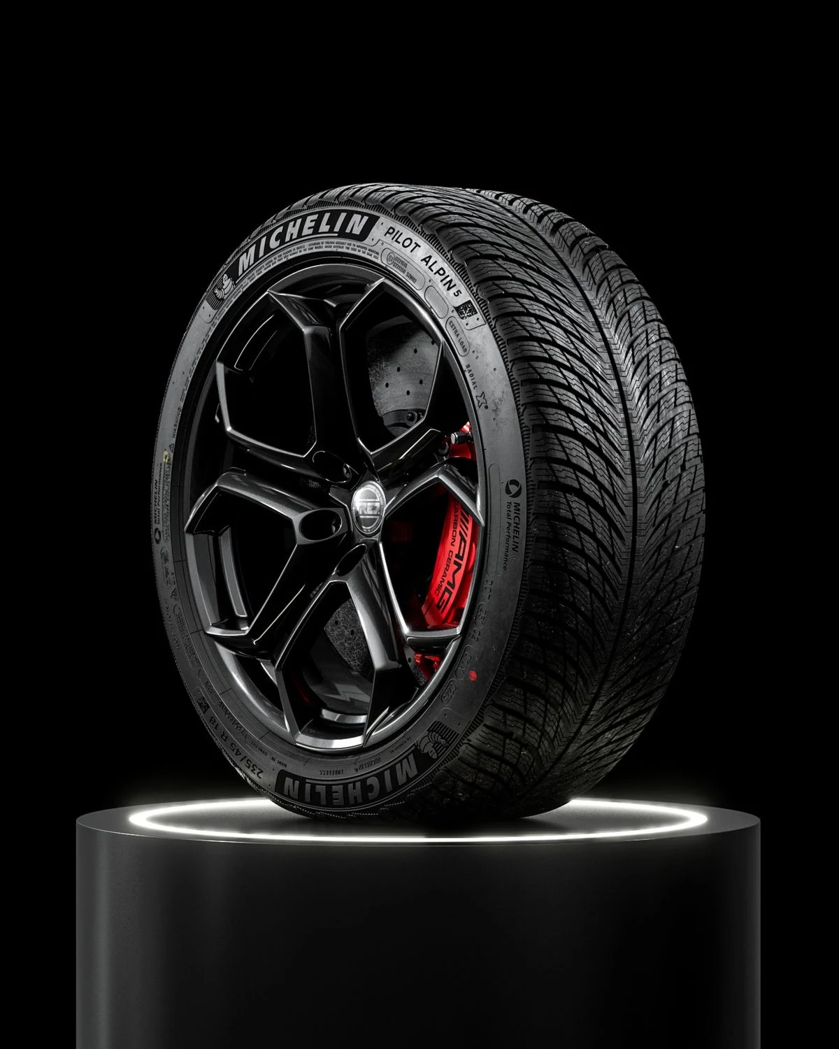 Pneu d'hiver Michelin sur jante noire, posé sur un socle lumineux